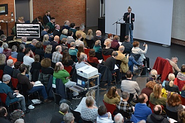 Vollbesetze Lichthalle im Kwadrat. Peter Litschke steht am Rednerpult.